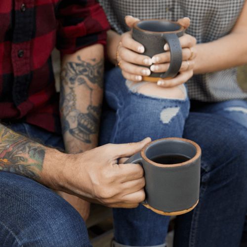 tattooed arm and womans hands holding mugs of coffee