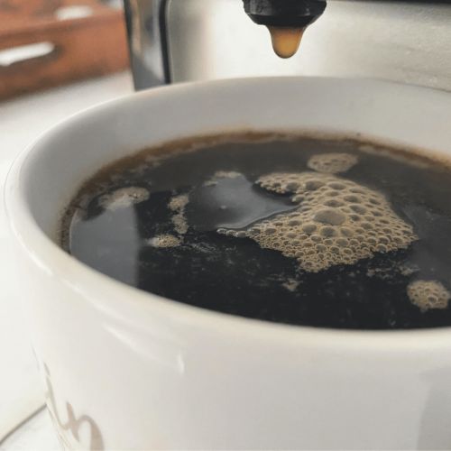 close up mug of coffee with keurig dripping above